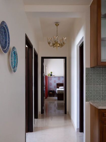 The hallway, styled with an elegant vintage chandelier and chic blue-toned ceramic wall plates. A wall adorned with travel trinkets adds a charming, personal touch.