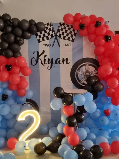 A close-up of the racing-themed backdrop with 'Two Fast Kiyan' text and balloon details.