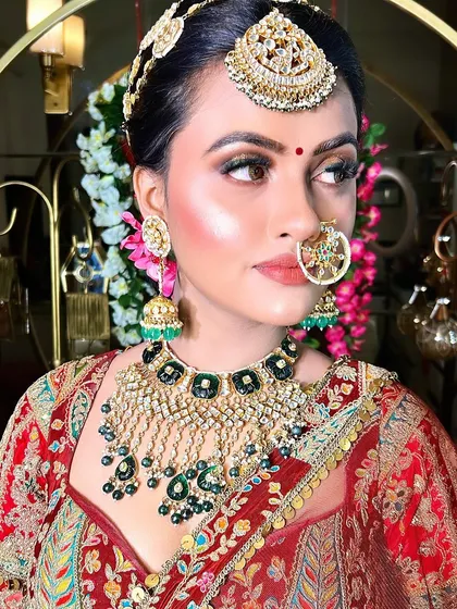 A beautiful portrait of a bride with striking green and gold jewelry. The makeup is designed to complement the jewelry, with a focus on glowing skin and defined eyes.