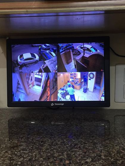 A compact monitoring setup on a countertop, showing a 4-camera view of the outside and inside of a property.