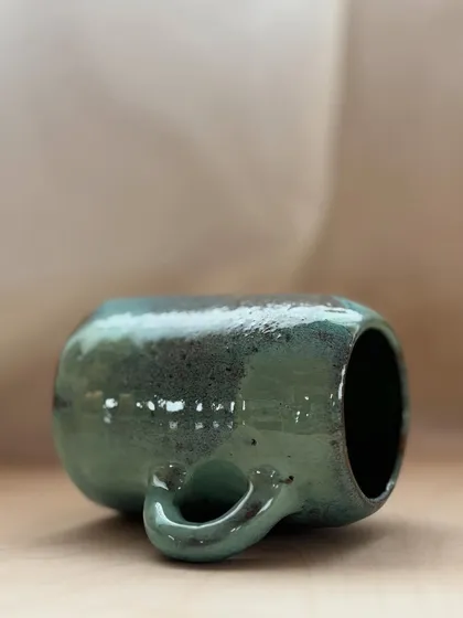 A student's beautifully glazed mug, with earthy green tones flowing over the surface.