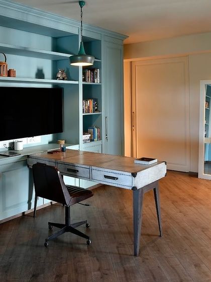A home studio needs to be both functional and inspiring. Here, a wall of custom-built shelves in a soft teal provides ample storage, while a simple desk and chair create a workspace that is calm and uncluttered.