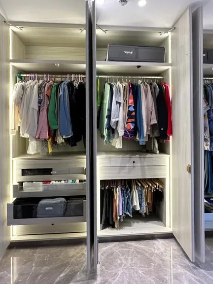 An open and airy walk-in closet featuring light wood tones and integrated lighting. Multiple sections are opened to showcase the sheer scale of the organization and the harmony between different zones.