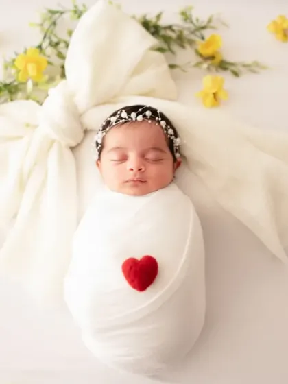 A simply beautiful shot of a newborn swaddled in white with a small red heart, surrounded by delicate yellow flowers. Sometimes the simplest concepts are the most powerful.