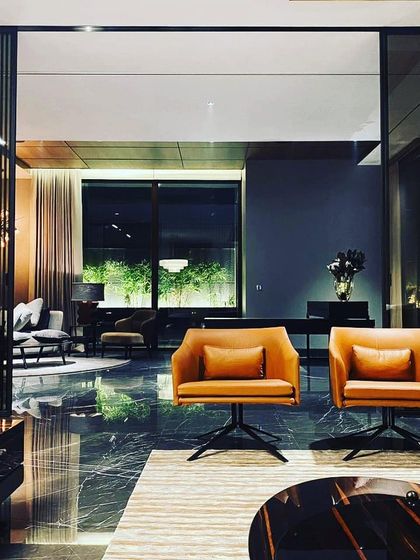 This formal living area in a Palam Vihar residence exudes moody sophistication. The lighting is intentionally kept low and warm, using pools of light from table lamps and accent fixtures to create intimate seating zones against a backdrop of softly lit curtains.