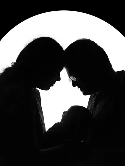 A beautiful silhouette of a new family, with the parents' heads touching as they hold their baby. This artistic shot creates a sense of intimacy and timelessness.