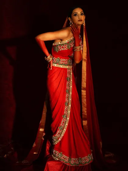 A statuesque pose showcasing the full length of the red saree and the long, flowing veil. The lighting is dramatic, carving the model out from the dark background.