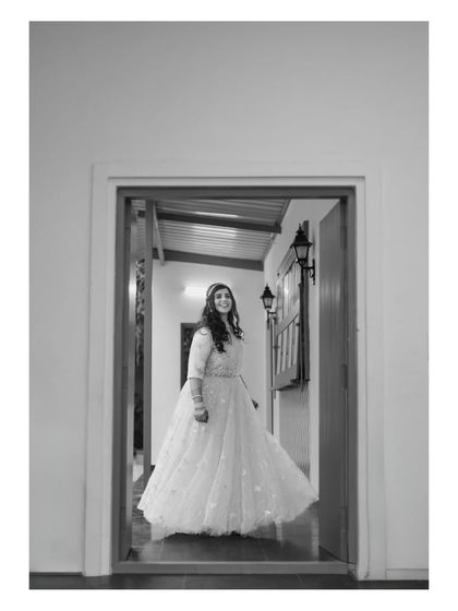 A black and white portrait of a bride in the doorway of a cottage. The composition creates a sense of anticipation and elegance.