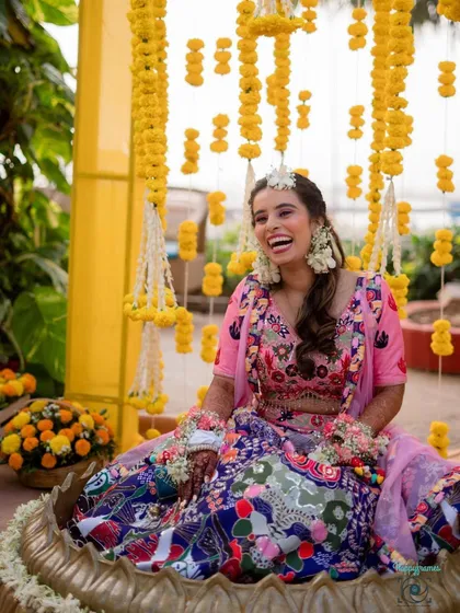 A candid shot of a bride enjoying her Mehendi ceremony. The decor features strings of marigolds, creating a classic and joyful backdrop for this happy occasion.
