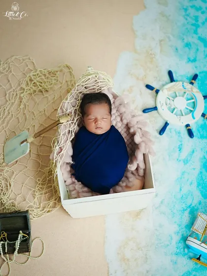 Our little sailor has arrived. This newborn is peacefully asleep in a boat-shaped prop, surrounded by a nautical theme with a ship's wheel, fishing net, and treasure chest. It's a creative way to announce your new arrival.