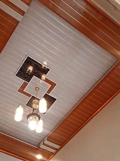A classic PVC panel ceiling with a wood-look border and a central decorative element. The chandelier adds a touch of traditional elegance to the modern material.