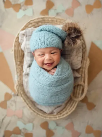 The biggest, happiest newborn smile! Capturing these unexpected moments of joy is what makes my job so special. This little one is cozy in a blue wrap and pom-pom hat.