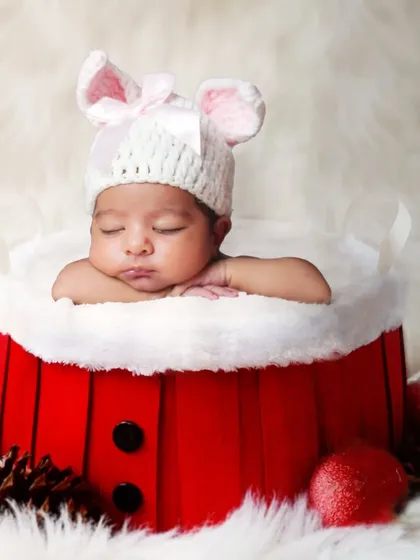 A close-up of a baby in a Santa-style basket, wearing a cute hat with bunny ears.