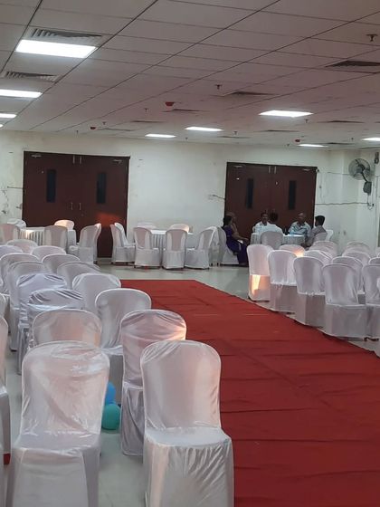 Rows of chairs with white covers and a red aisle carpet, ready for a formal event in a hall.