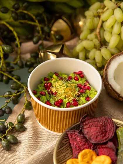 A vibrant green pea dip topped with pomegranate seeds and sev, served with vegetable chips, offering a modern twist on Indian appetizers.