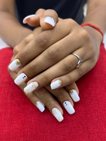 This chic and modern nail design features a clean white base with delicate gold geometric patterns and black dot accents. It's a perfect example of minimalist yet stylish nail art.