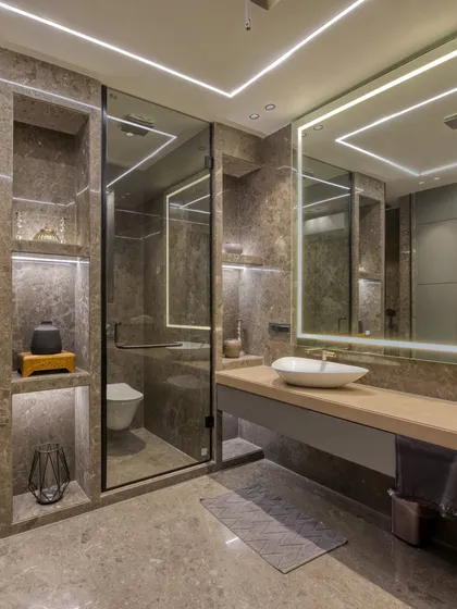 A modern bathroom design featuring large-format tiles, a floating vanity, and integrated linear LED lighting. The built-in, backlit shelving adds both storage and a soft, ambient glow.