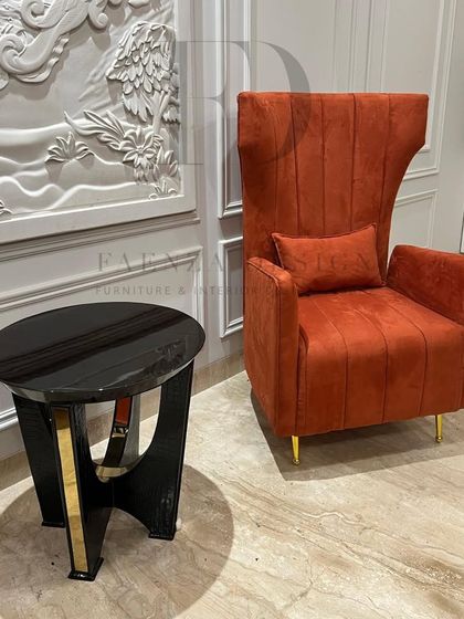A close-up of the burnt orange high-back chair and the accompanying side table. The table's V-shaped base with gold accents echoes the luxurious feel of the chair.