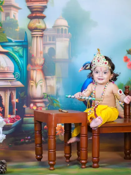 This Little Krishna is ready to play his flute, sitting happily on a small stool in our vibrant Vrindavan setup. A playful and charming portrait.