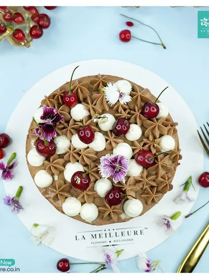 A classic Black Forest cake, generously decorated with fresh cherries, chocolate frosting, and dollops of fresh cream. It's a timeless choice for any celebration.
