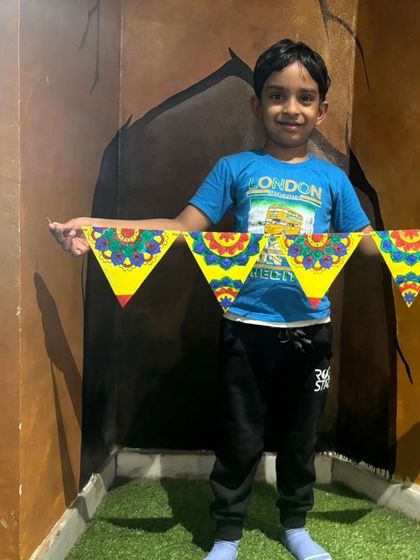 A young boy proudly displays the colorful banner he created during our Dusshera camp, showcasing his artistic skills.