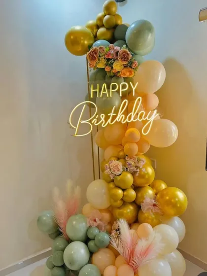 A beautiful and delicate balloon column in pastel and gold tones, with a "Happy Birthday" neon sign.