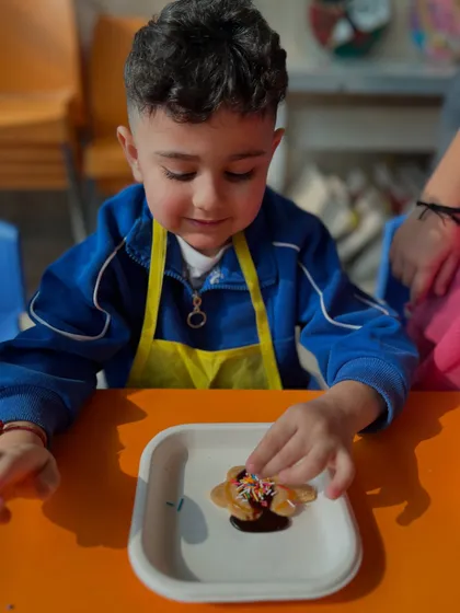 A smiling boy adds sprinkles to his chocolate-covered cookie.