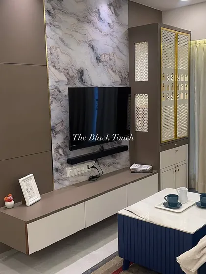 This view showcases the elegant TV unit with a marble-finish backdrop and an integrated mandir with intricate jali work. The design balances modern entertainment needs with traditional elements, creating a unique focal point in the living room.