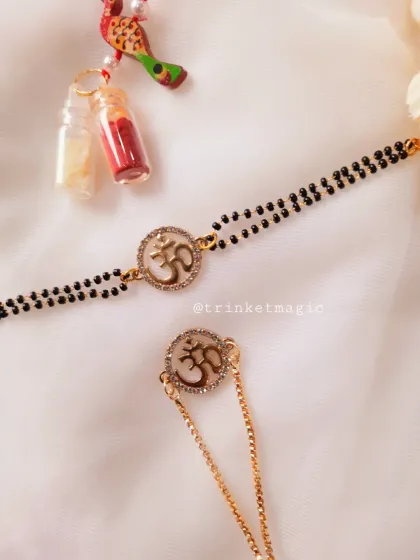 This set blends tradition with modern spirituality. The Om symbol is set in a crystal-studded circle on a mangalsutra-style bracelet for bhabhi and a matching chain Rakhi for bhai.
