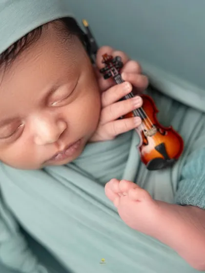 A tiny musician in the making. This close-up shot features a newborn holding a miniature violin, a creative way to incorporate a family's passion for music into the session.