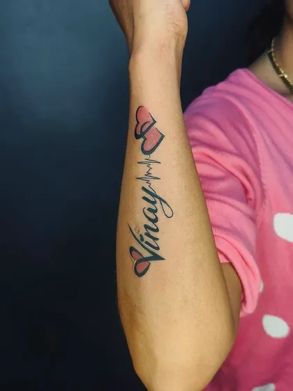 Another view of the "Vinay" name tattoo with color, showing how it looks on the arm. The placement along the forearm is perfect for this style.