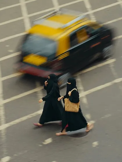 A colored version of the aerial shot of two women crossing the street. The motion-blurred taxi adds a dynamic element, contrasting with the steady pace of the pedestrians.