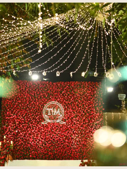 A beautiful shot of the red rose wall, framed by the natural foliage and fairy lights. It shows how a single, powerful decor element can define the entire atmosphere of an event.
