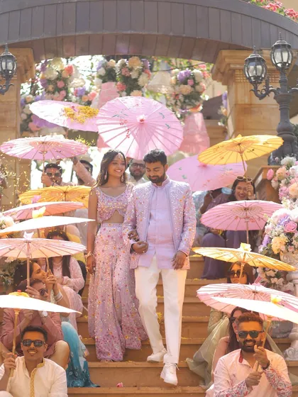 The couple makes a grand entrance down a staircase lined with flowers and guests holding colorful umbrellas. This coordinated entry created a stunning visual for their pastel-themed carnival.