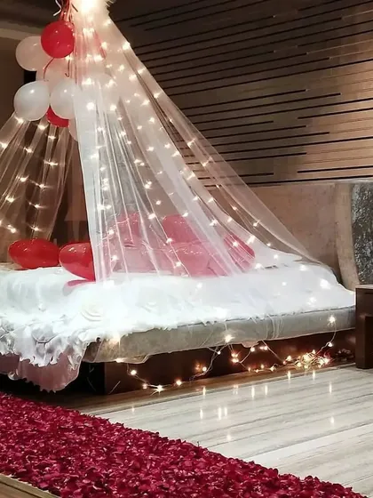 The details make the difference. Here, a beautiful canopy with fairy lights creates a cozy focal point over the bed, while a path of red rose petals on the floor adds a layer of classic romance to the room.