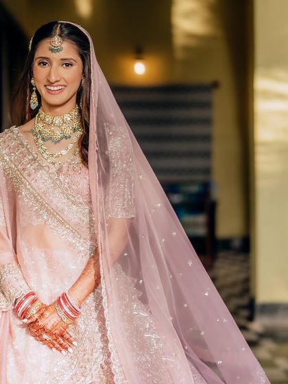 This bride glows in her soft pink lehenga. The makeup is kept fresh and luminous, with a focus on dewy skin and subtly defined eyes to match her elegant and modern bridal style.