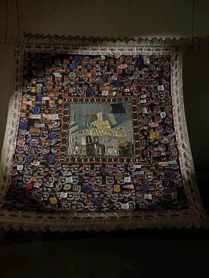 A large, intricately detailed textile piece from 'WEAVING LIGHT', spotlit in the dark.