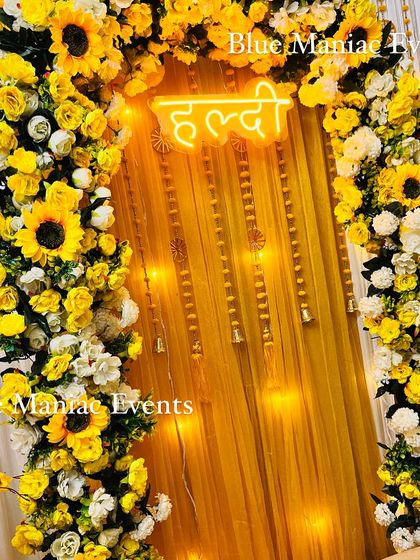 A close-up of the sunflower Haldi arch, highlighting the vibrant yellow flowers and the warm glow of the neon sign.
