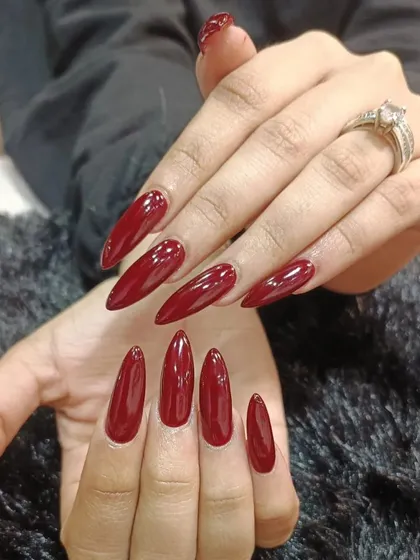 A dramatic set of extra-long stiletto nails in a deep, glossy red polish.