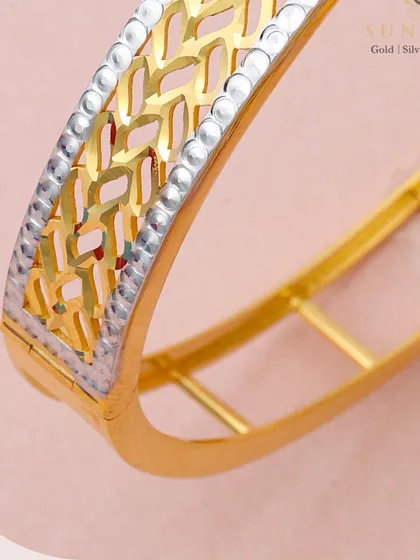 A detailed shot of the wide, two-tone gold kada, highlighting the precision of the cut-out pattern and the textured border. This piece combines traditional width with a modern aesthetic.
