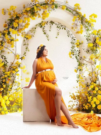 A radiant portrait featuring a mom-to-be seated amidst a stunning arch of yellow flowers. The matching yellow halter gown and floral crown create a bright and joyful bohemian-inspired look.