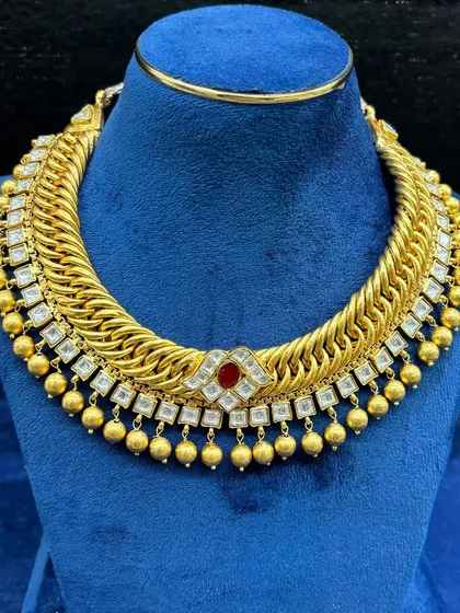 Another variation of our popular gold-plated sutarla necklace. This one features a central red stone and hanging kundan drops, perfect for a classic wedding look.