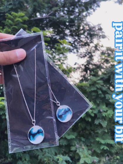 This set of two matching 'wave' necklaces is perfect for best friends. The design mimics ocean waves using blue and white pigments, sealed in a circular silver-tone pendant.