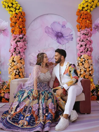 The couple seated against a beautiful floral backdrop, creating a picture-perfect wedding stage portrait.