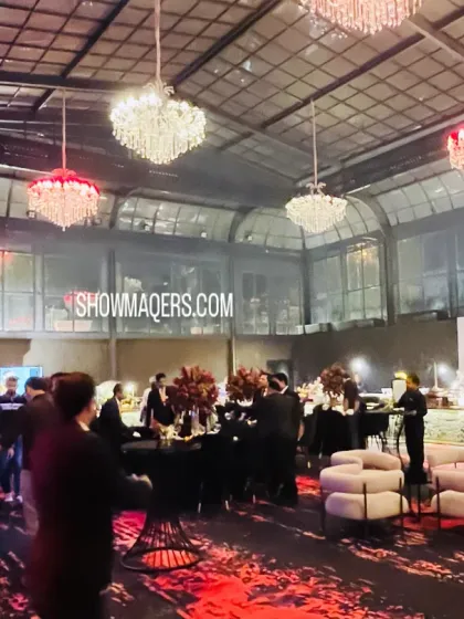 A wide shot of a dramatic cocktail event in a glasshouse venue. The decor features a striking black and red color palette, with crystal chandeliers adding a touch of glamour.