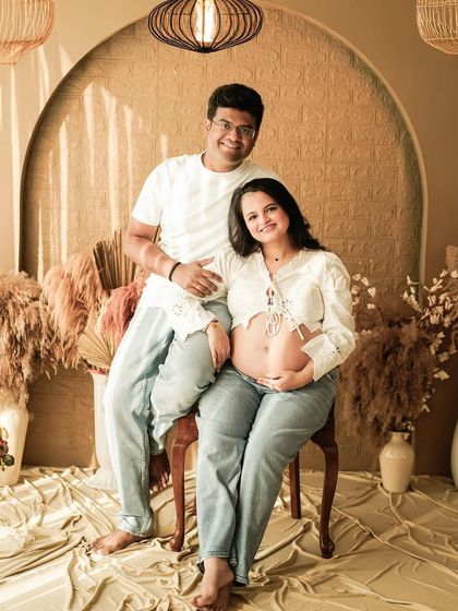 A beautiful portrait of a couple in a casual, boho-inspired studio setting. The mom-to-be's exposed bump and jeans create a modern and authentic look.