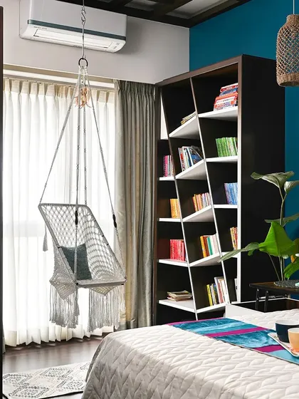 We love creating personal nooks that tell a story. This cozy reading corner features a custom-built asymmetrical bookshelf, a comfortable macrame swing chair, and a vibrant teal accent wall, making it the perfect weekend retreat within your own home.