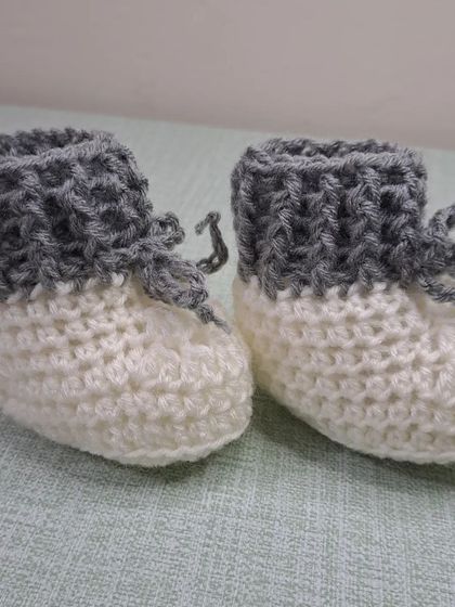 A front view of the two-tone grey and white booties, a perfect handmade gift for any baby.