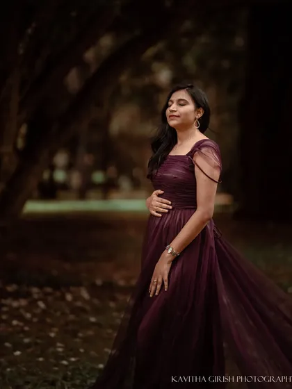 A quiet, reflective moment during an outdoor maternity shoot. The soft focus of the background and the gentle pose create a feeling of peace and contentment.