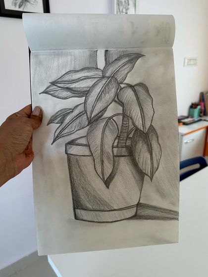 A student holds up their finished sketch of a potted plant, showing great texture in the leaves.